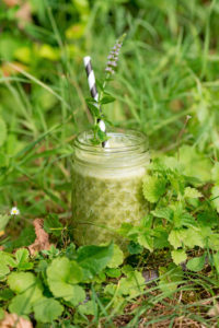 Glas mit grünem Smoothie, Strohhalm und Minzblüte steht auf bewachsened Boden Glas mit grünem Smoothie, Strohhalm und Minzblüte steht auf bewachsened Boden